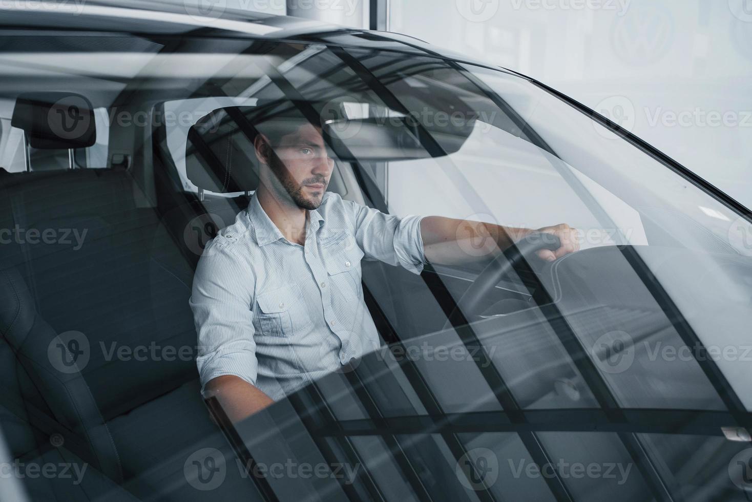 un giovane siede in un'auto appena acquistata tenendo le mani su un timone. foto