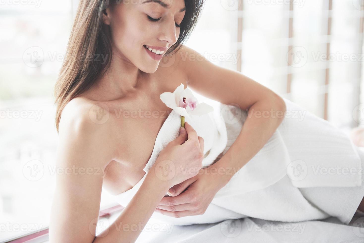 bella giovane donna che si rilassa su un asciugamano con un fiore di orchidea isolato su uno sfondo bianco foto