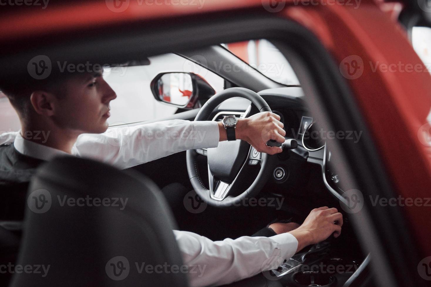 un giovane siede in un'auto appena acquistata tenendo le mani su un timone foto