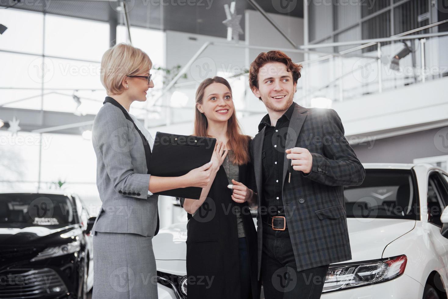 comprando la loro prima auto insieme. vista dall'alto del giovane venditore di auto in piedi presso la concessionaria che racconta le caratteristiche dell'auto ai clienti foto