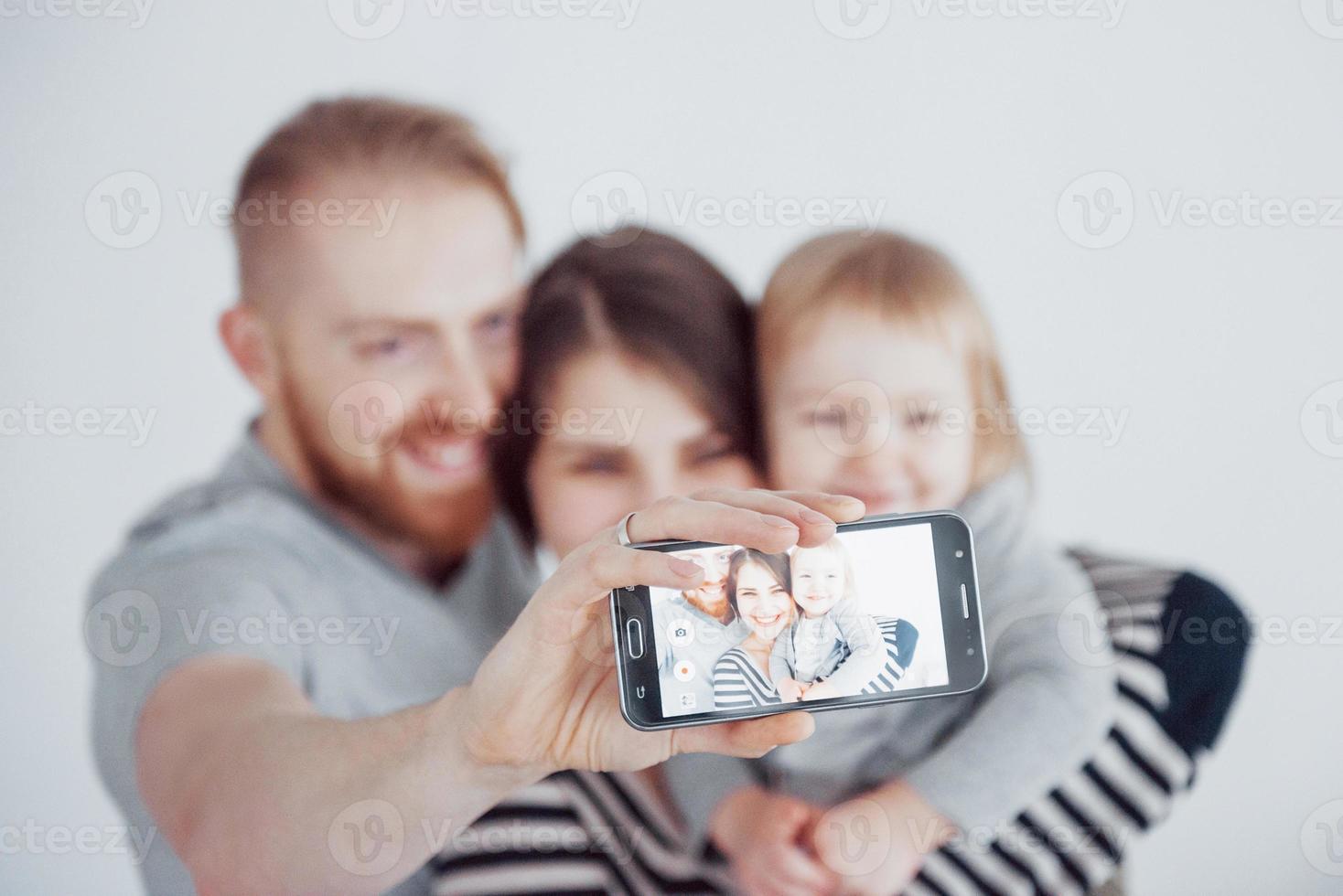 famiglia, vacanze, tecnologia e persone - madre, padre e bambina sorridenti che fanno selfie con la fotocamera su sfondo bianco foto