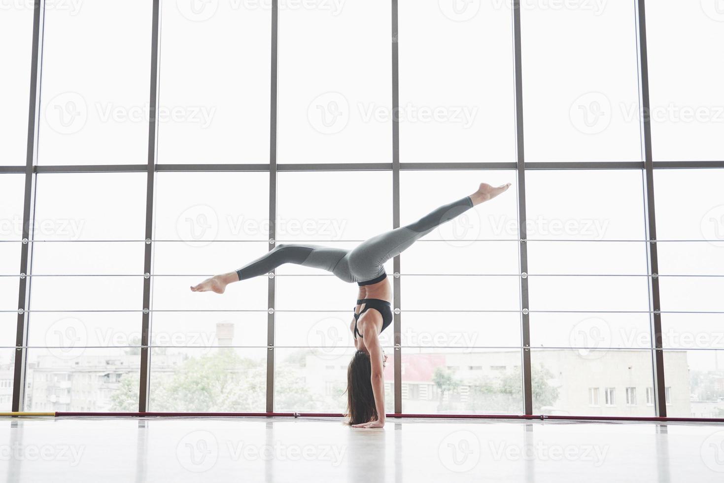 una sportiva sportiva che sta facendo lezioni di yoga, allungando le gambe vicino alla grande finestra foto