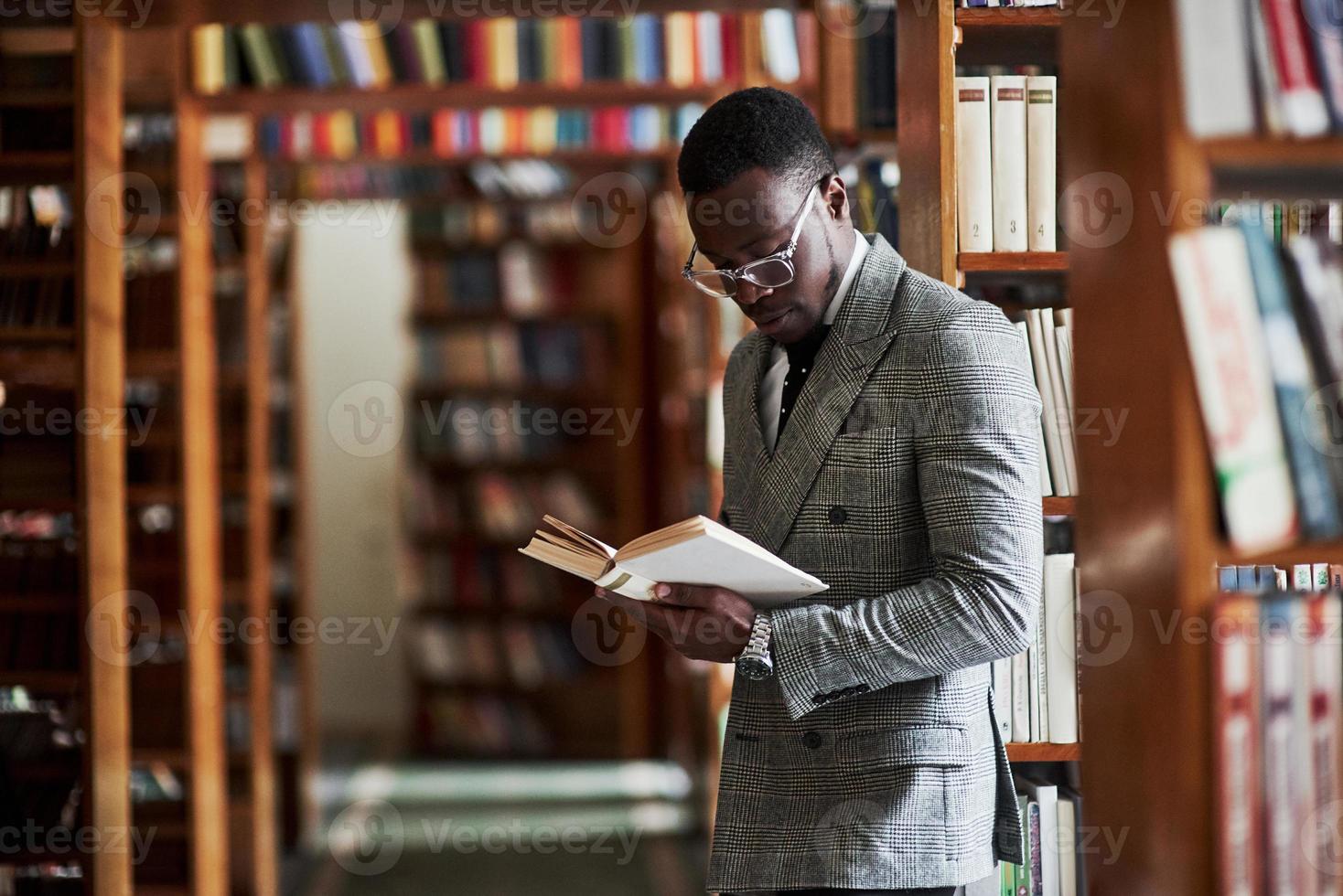 un uomo afroamericano in giacca e cravatta in piedi in una biblioteca nella sala di lettura. foto