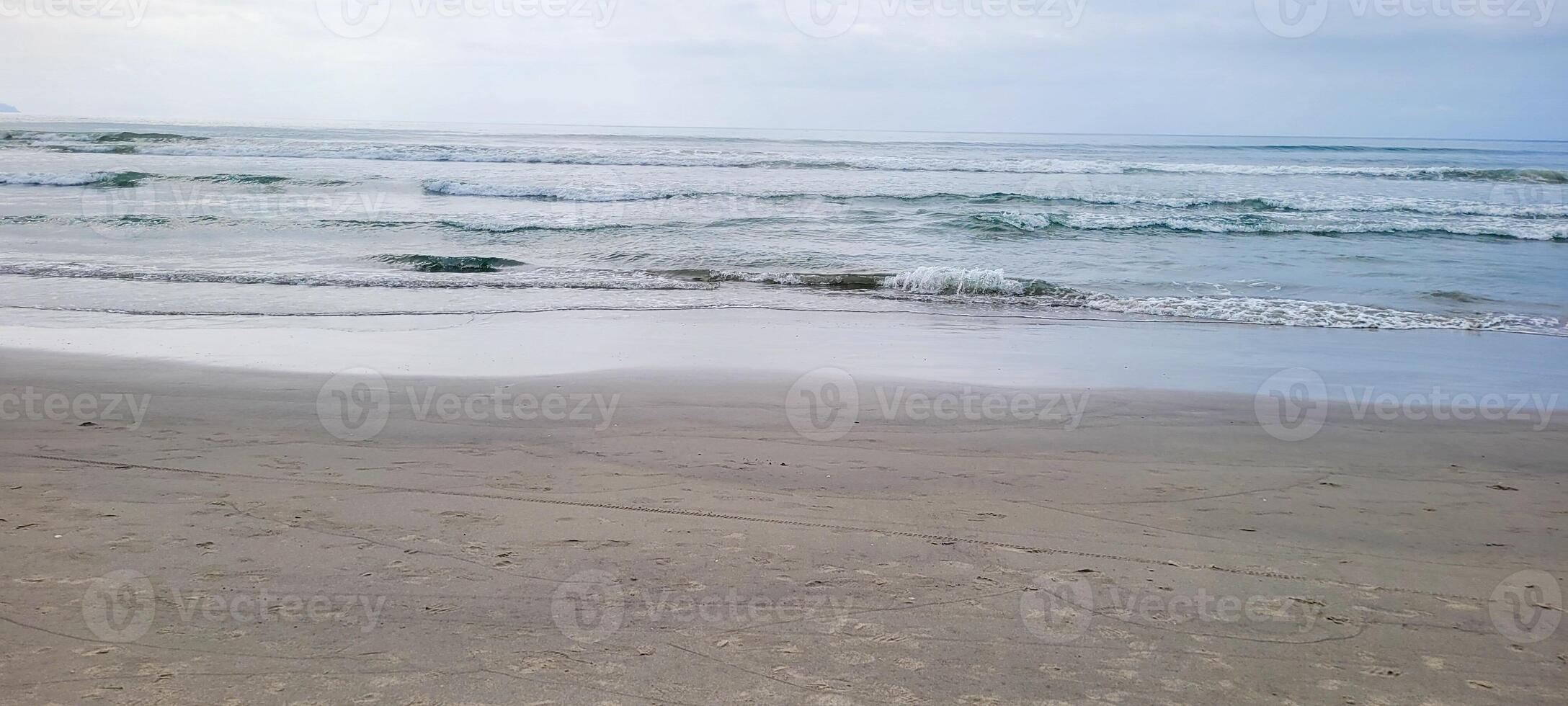 Immagine di spiaggia con bianca sabbia e calma mare su soleggiato giorno con bagnanti e surfers su il spiaggia foto