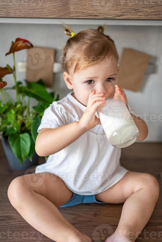 contento bambino ragazza seduta a il tavolo nel il cucina e potabile latte foto