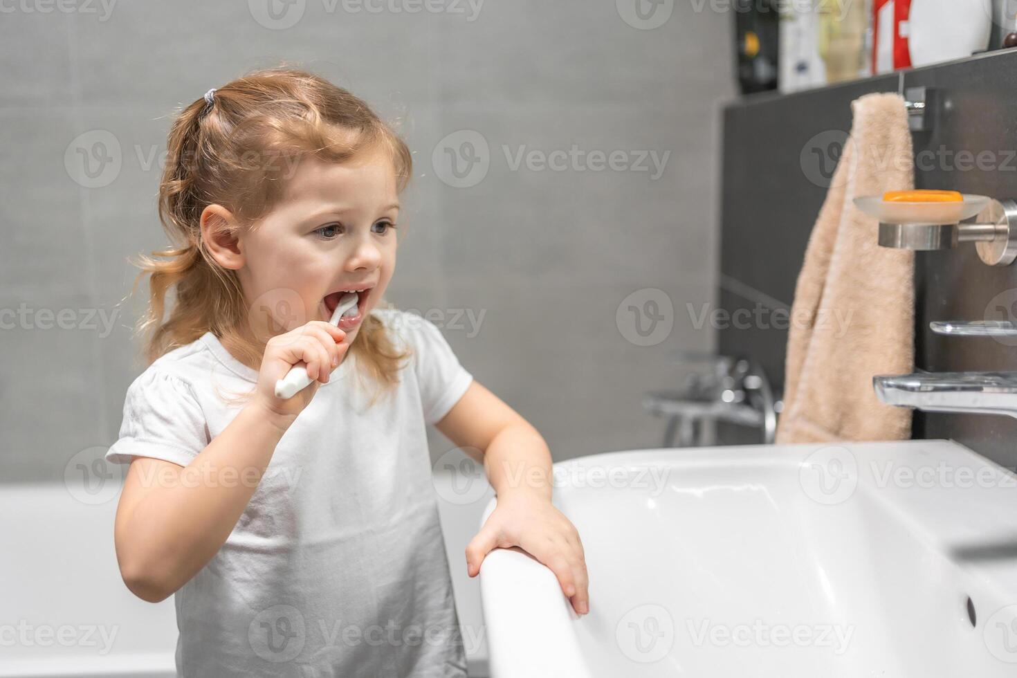 contento bambino piccolo ragazza spazzolatura denti nel il bagno foto