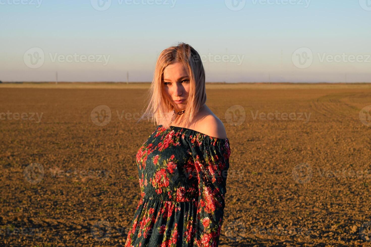 donna nel un' arato campo nel un' rosso nero vestito su un' tramonto sfondo. foto