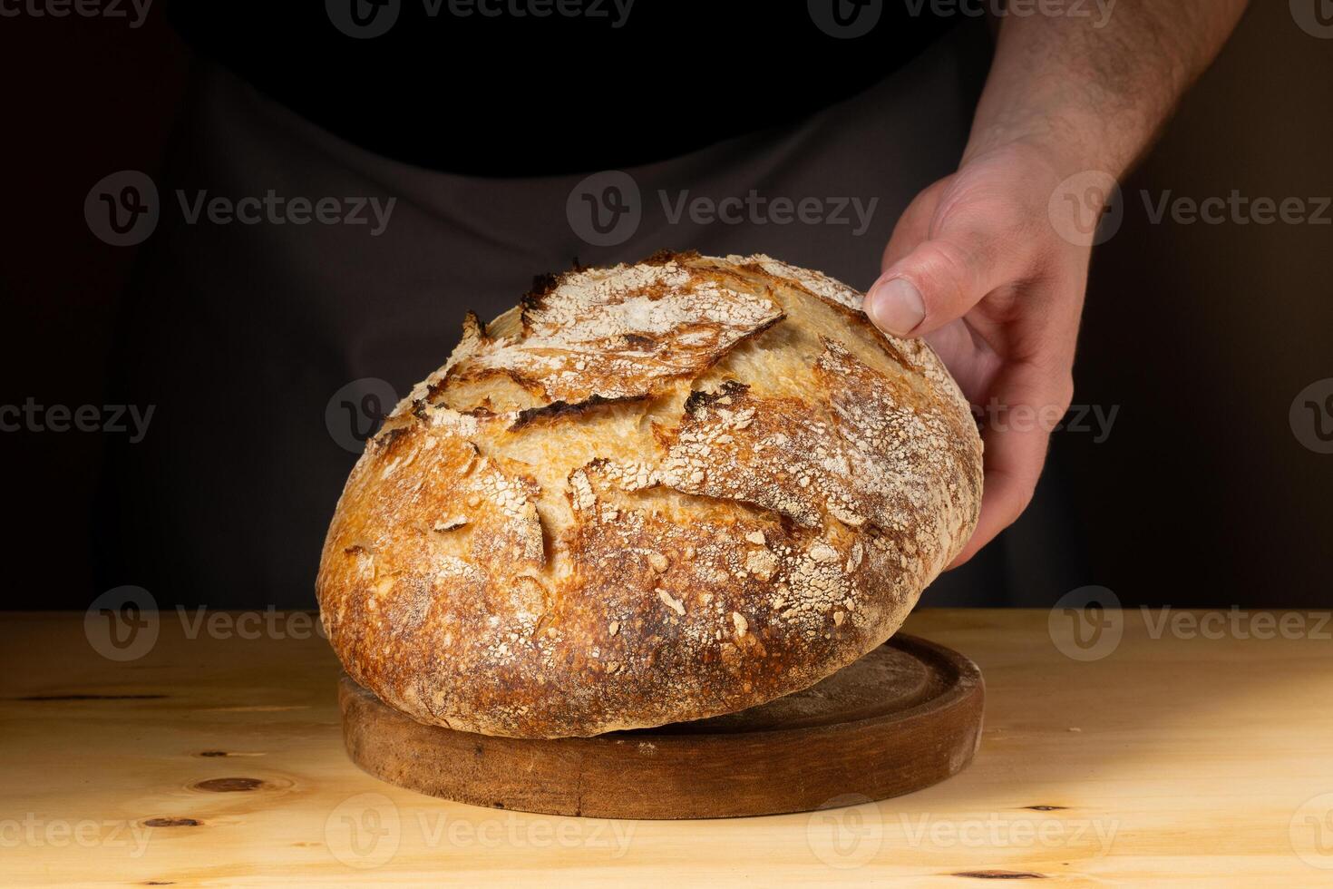 il mani di un' giovane uomo maneggio lievito pane, evidenziazione il pane con bellissimo d'oro toni contro il buio sfondo. foto