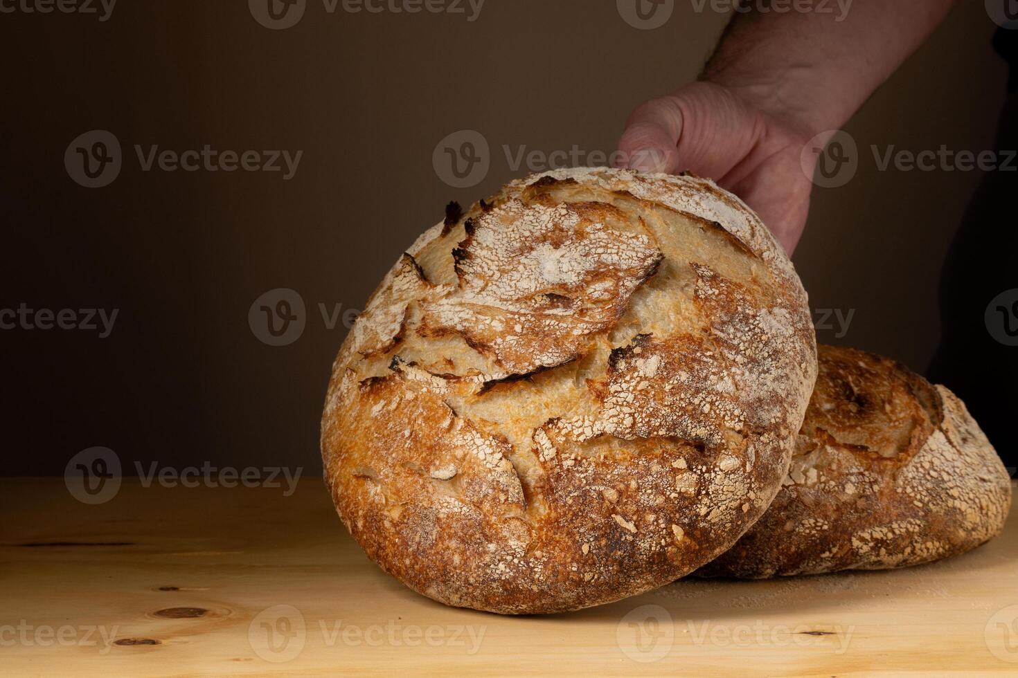 il mani di un' giovane uomo maneggio lievito pane, evidenziazione il pane con bellissimo d'oro toni contro il buio sfondo. foto