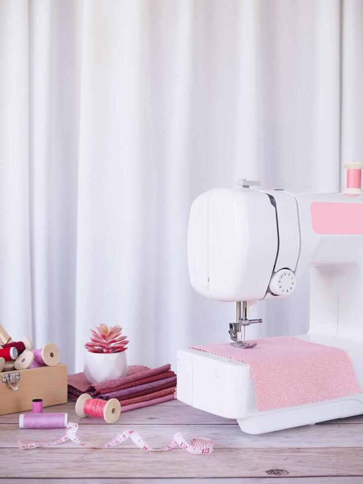 vicino su cucire macchina Lavorando con rosa tessuto, cucire Accessori su il tavolo, punto nuovo vestiario. foto