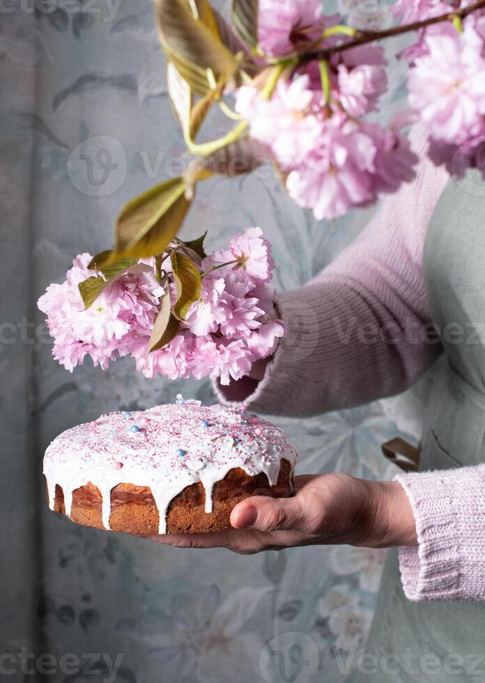 un' donna decora un' fatti in casa Pasqua torta con rosa sakura fiori, primavera fiorire foto