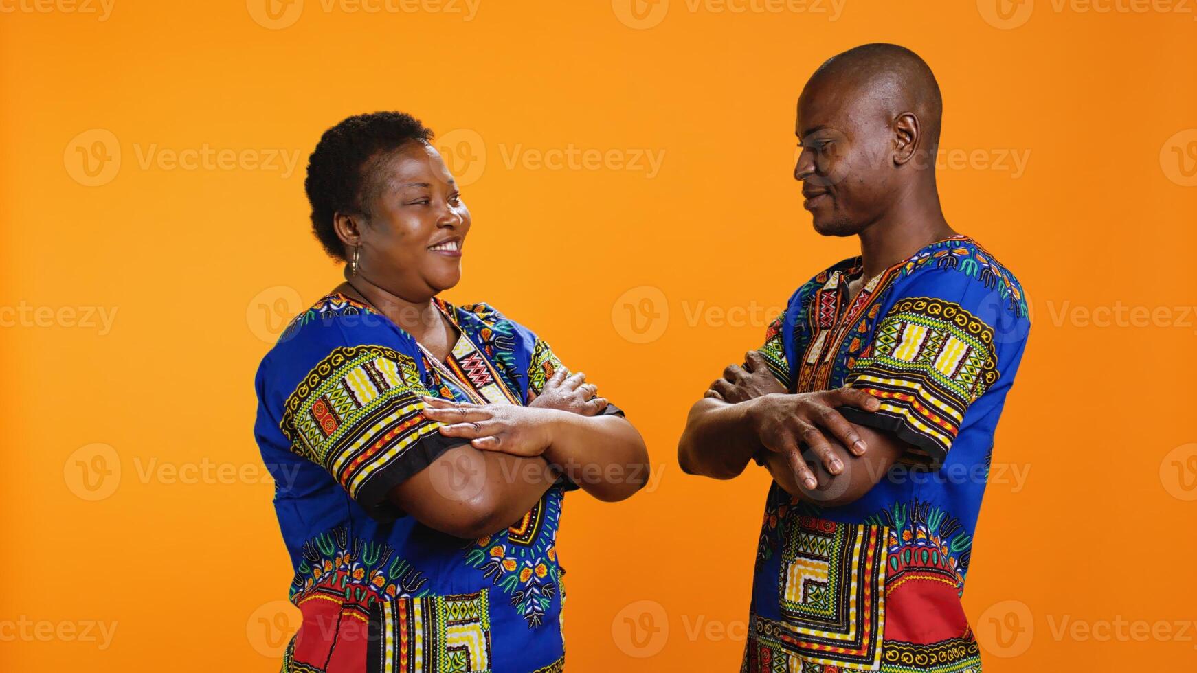 fiducioso sposato persone in posa su telecamera con colorato abbigliamento, in mostra tradizionale africano americano capi di abbigliamento e essere orgoglioso di loro cultura. gioioso marito e moglie con braccia incrociato. foto