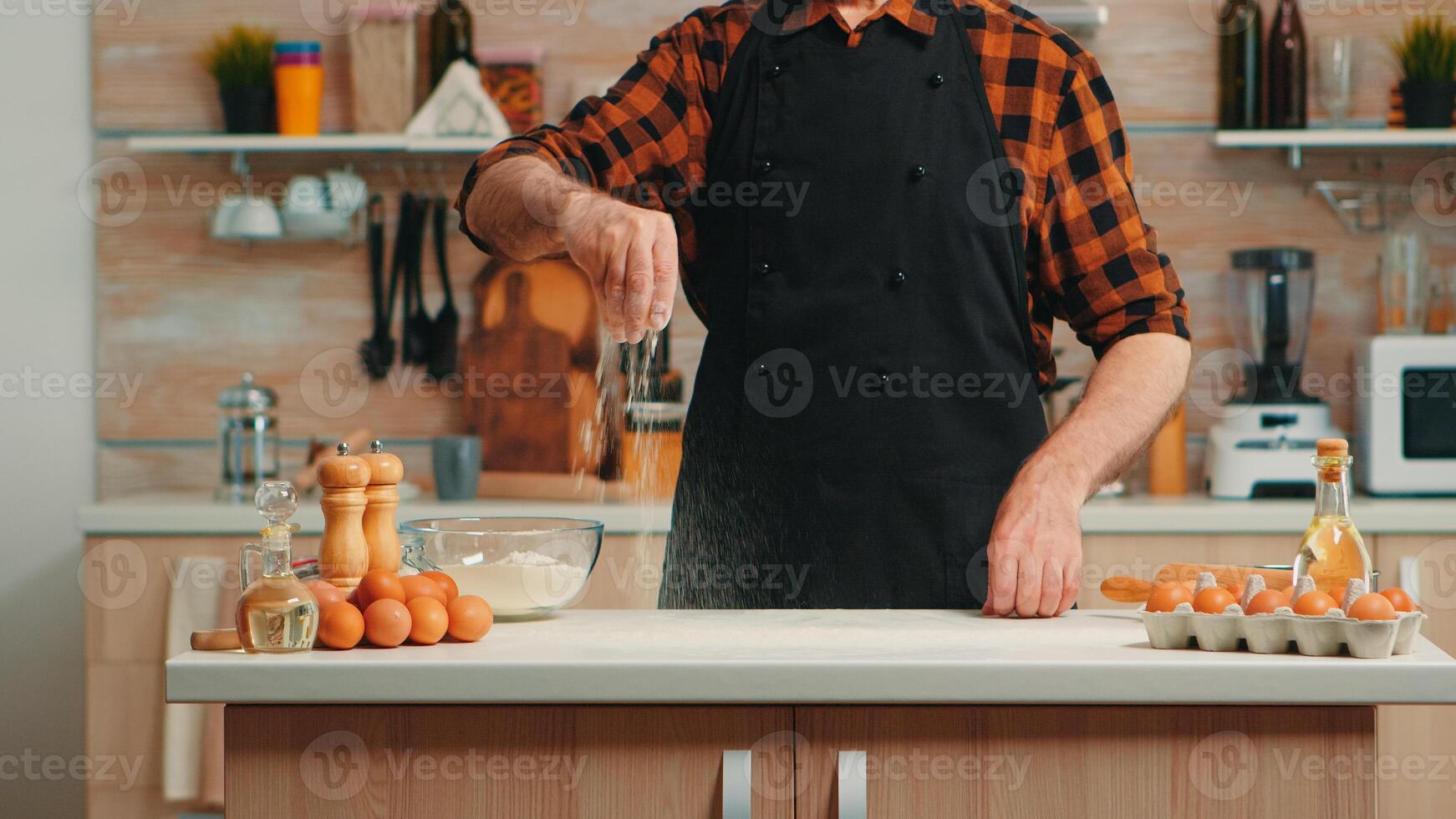 esperto capocuoco panettiere utilizzando Grano Farina diffusione esso per cibo preparazione. pensionato anziano uomo con bonete e grembiule aspersione setacciare vagliatura ingredienti di mano cottura al forno fatti in casa Pizza e pane foto