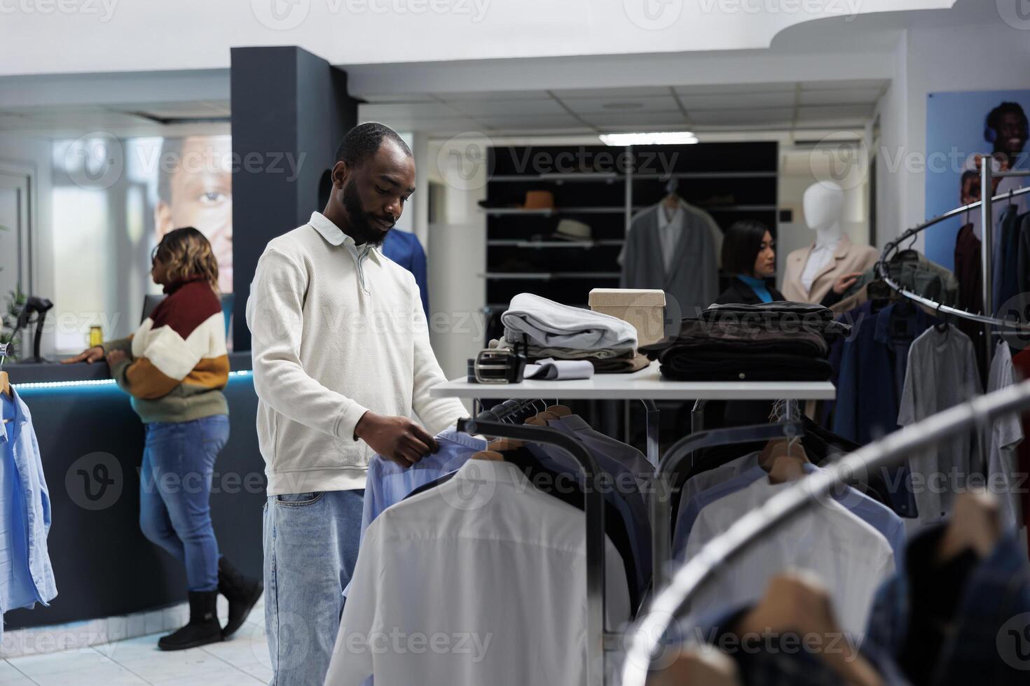giovane africano americano uomo shopping per casuale abbigliamento e navigazione cremagliera con camicie nel abbigliamento maschile boutique. capi di abbigliamento memorizzare cliente la scelta attrezzatura e controllo indumento stile foto