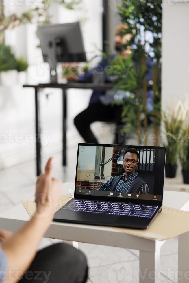 esecutivo su il computer portatile schermo ascoltando per dipendente presentazione attraverso video chiamata. progetto manager avendo in linea incontro con africano americano collega nel coworking spazio foto