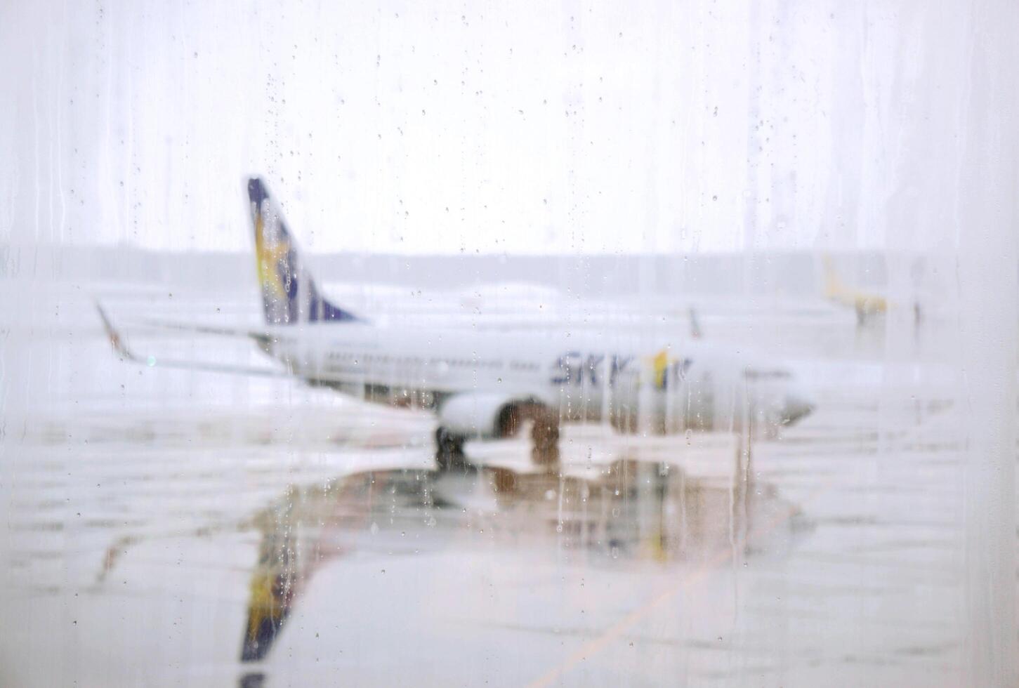 hokkaido, Giappone, 2023 - sfocato gocce di pioggia su terminale dell'aeroporto finestre con il cielo linea aerea aereo parcheggiata su bagnato pista di decollo e nebbioso tempo metereologico sfondo. foto