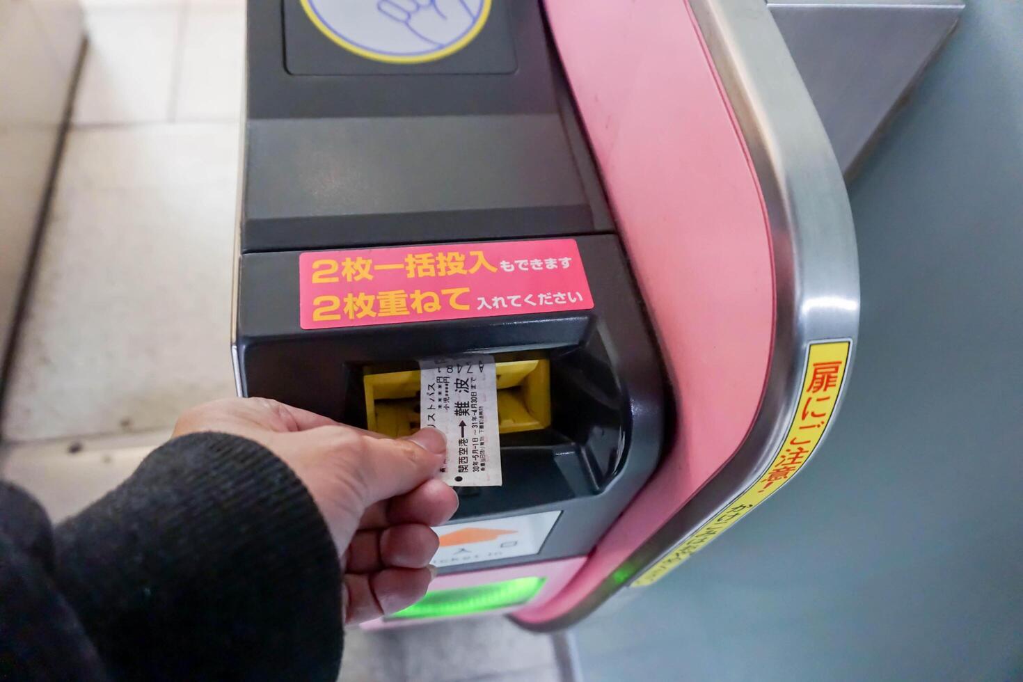 osaka città, Giappone, 2023- avvicinamento mano di persone inserire metropolitana biglietto nel il Ingresso automatico biglietto macchine a numba metropolitana stazione, osaka, Giappone. foto