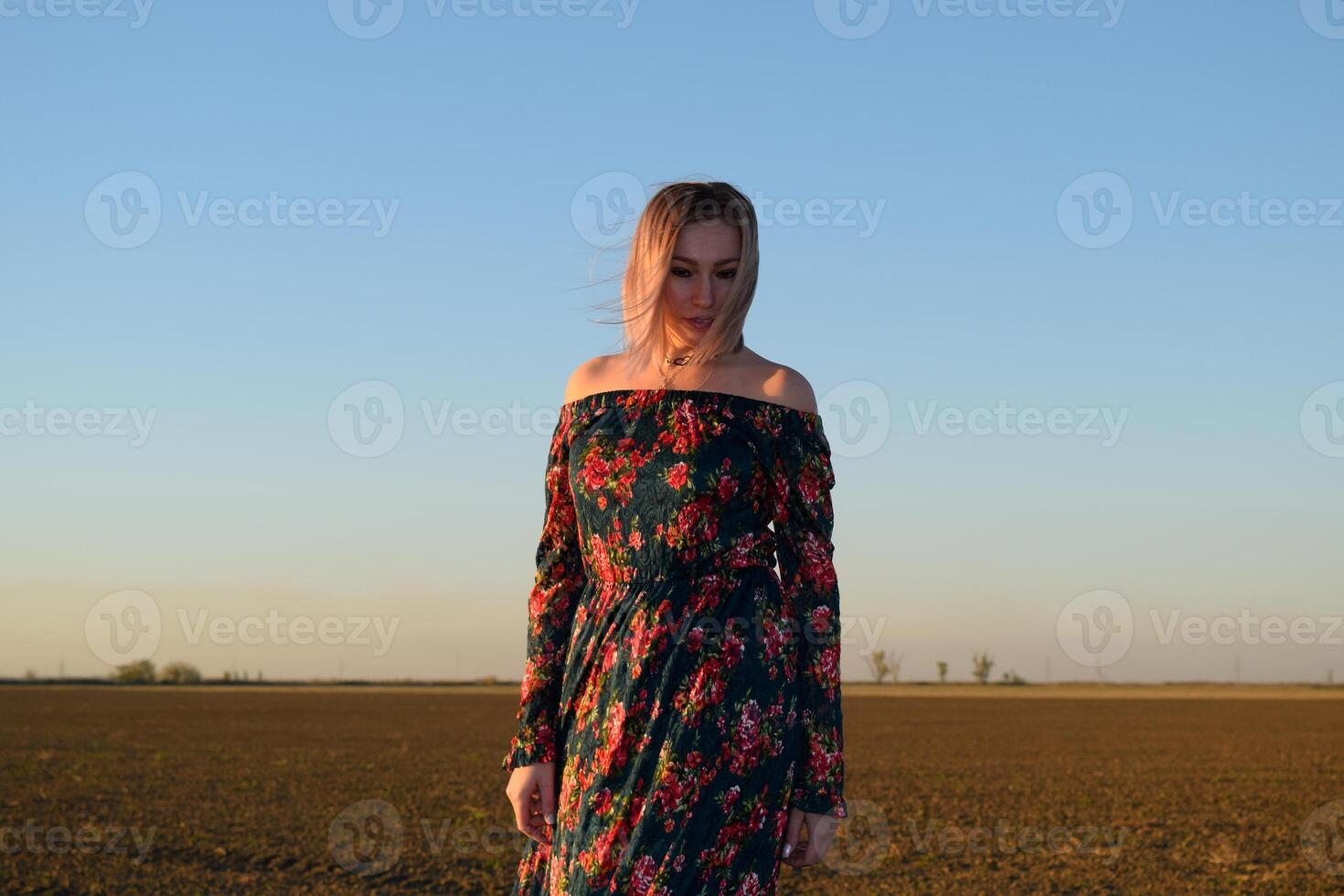 donna nel un' arato campo nel un' rosso nero vestito su un' tramonto sfondo. foto