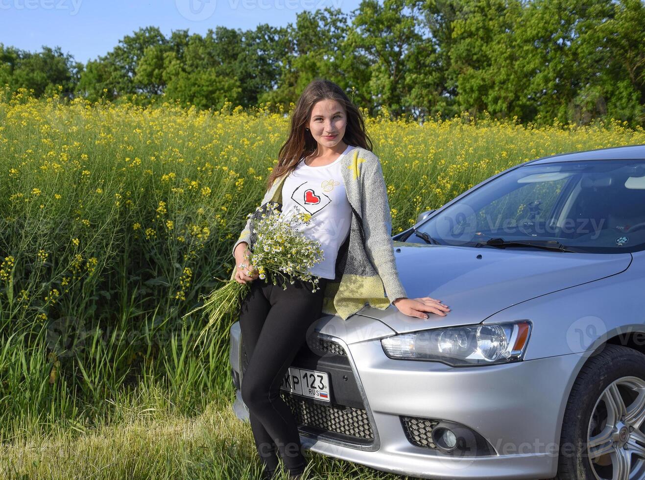 un' bellissimo giovane donna con un' mazzo di margherite sta vicino un' argento auto foto