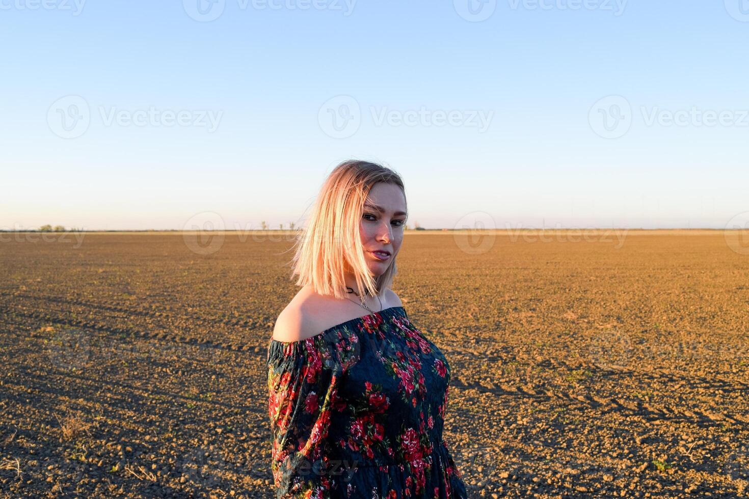 donna nel un' arato campo nel un' rosso nero vestito su un' tramonto sfondo. foto