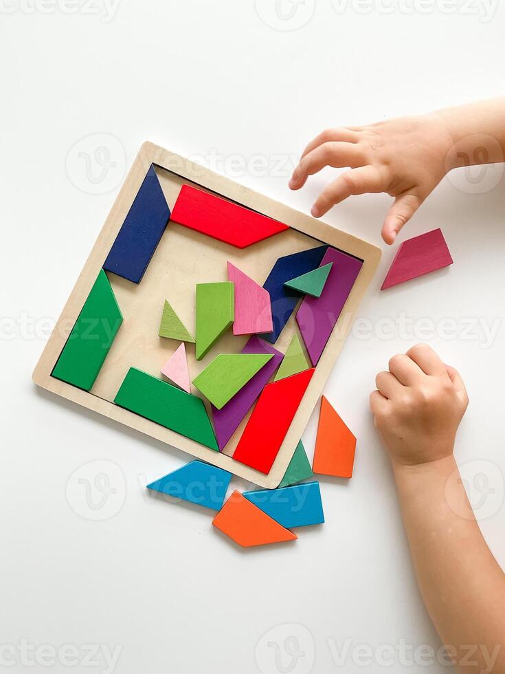 Childs mano raccoglie multicolore di legno mosaico su bianca sfondo. bambino risolve colorato tangram foto
