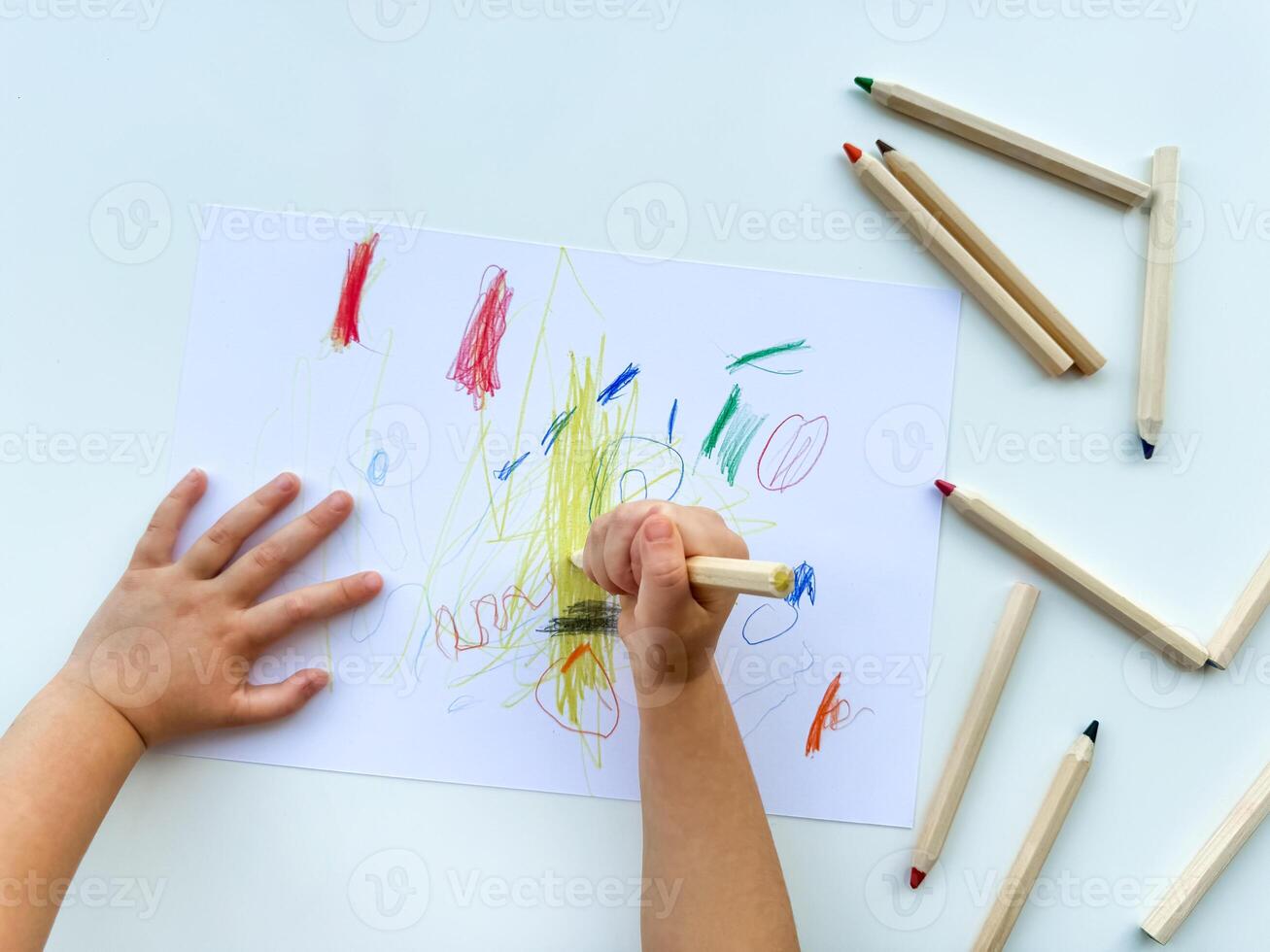 piccolo bambino disegna con colorato matite su carta su bianca tavolo. foto