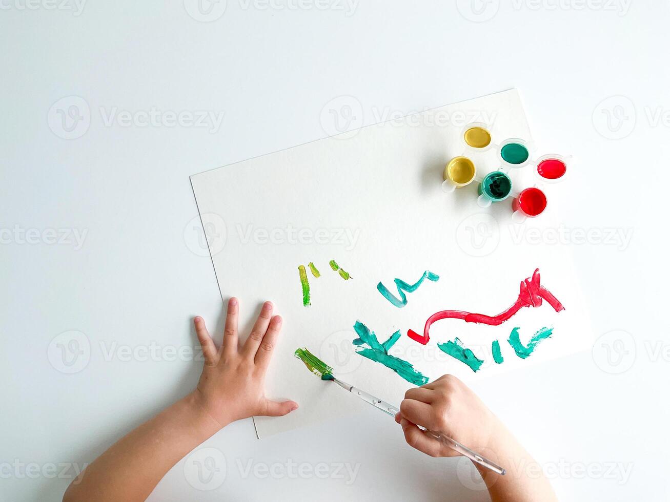 piccolo bambino disegna con vernici e spazzola su bianca tavolo. foto