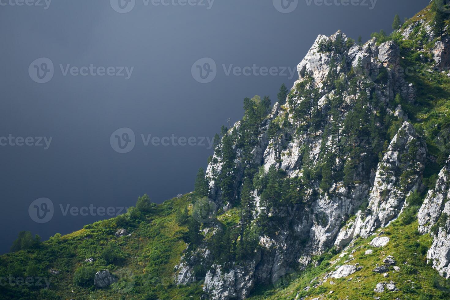 montagna paesaggio - un' roccia illuminato di il sole e un' cupo nube dietro a esso foto