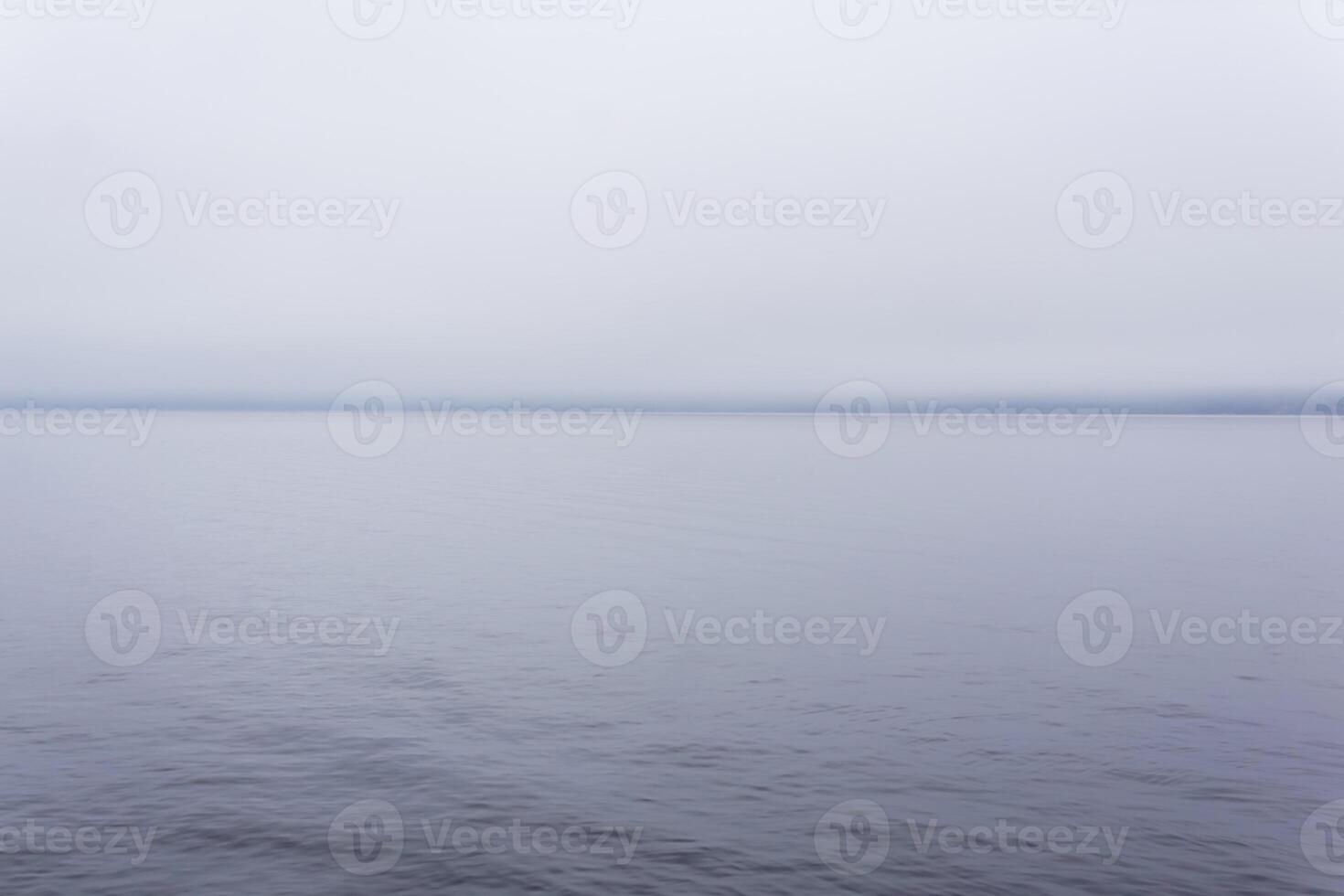 freddo corpo di acqua con un' lontano riva nascosto di nebbia foto