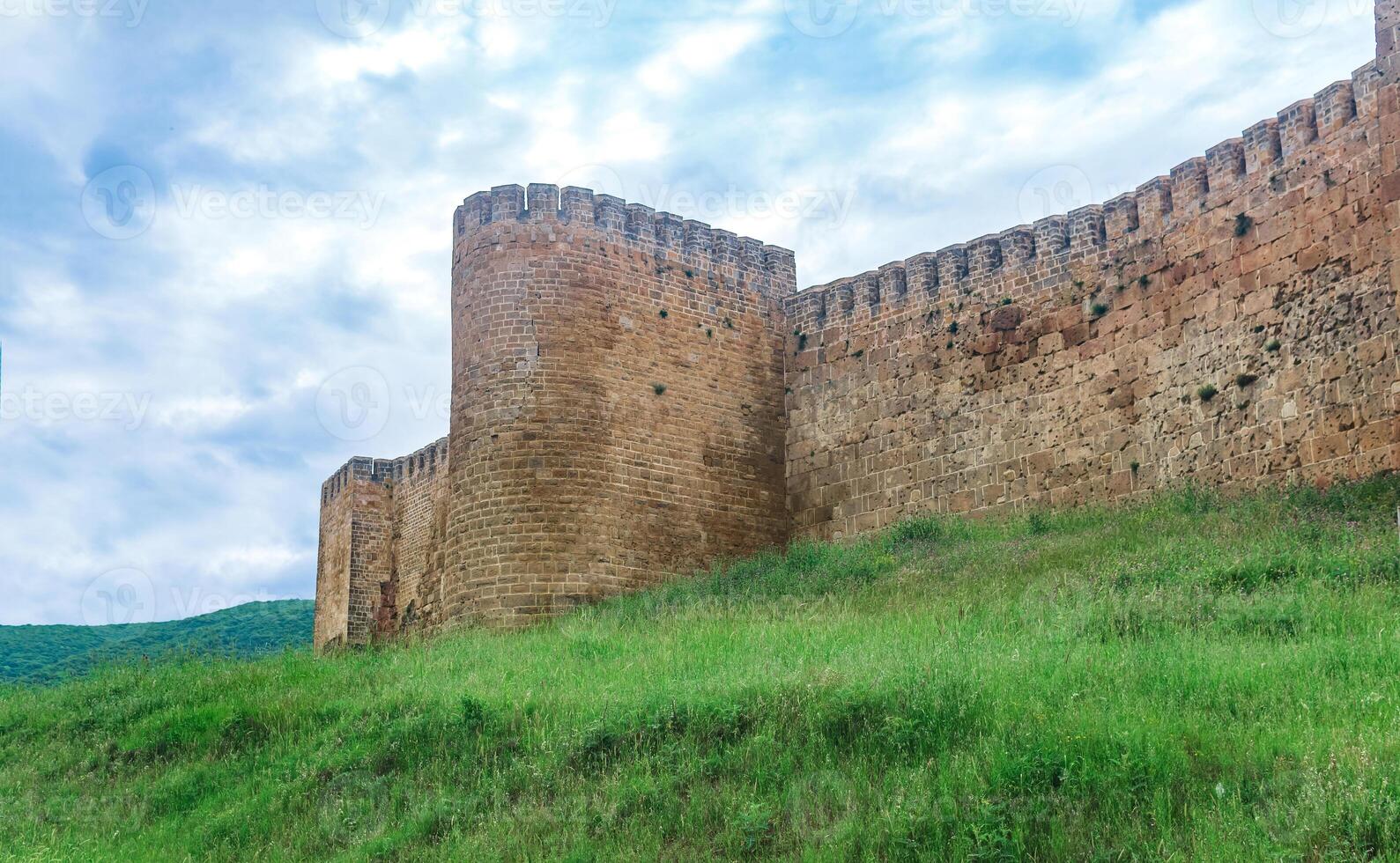 parete di un' medievale fortezza sopra un' bastione coperto di vegetazione con erba contro il colline e cielo, naryn-kala cittadella nel derbent foto