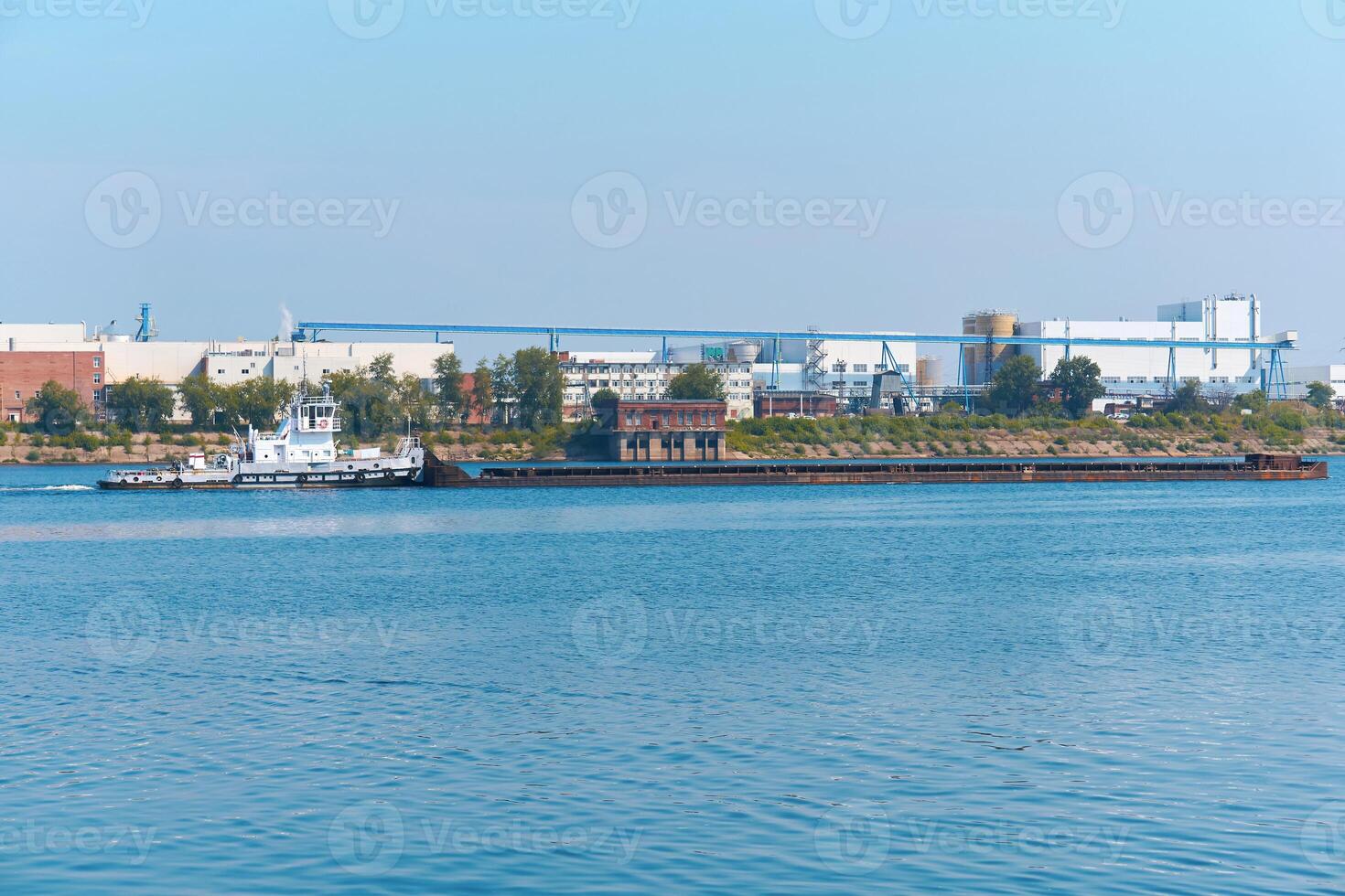 rimorchiatore spinge asciutto massa carico chiatta su il fiume contro il fondale di un industriale paesaggio su il riva foto