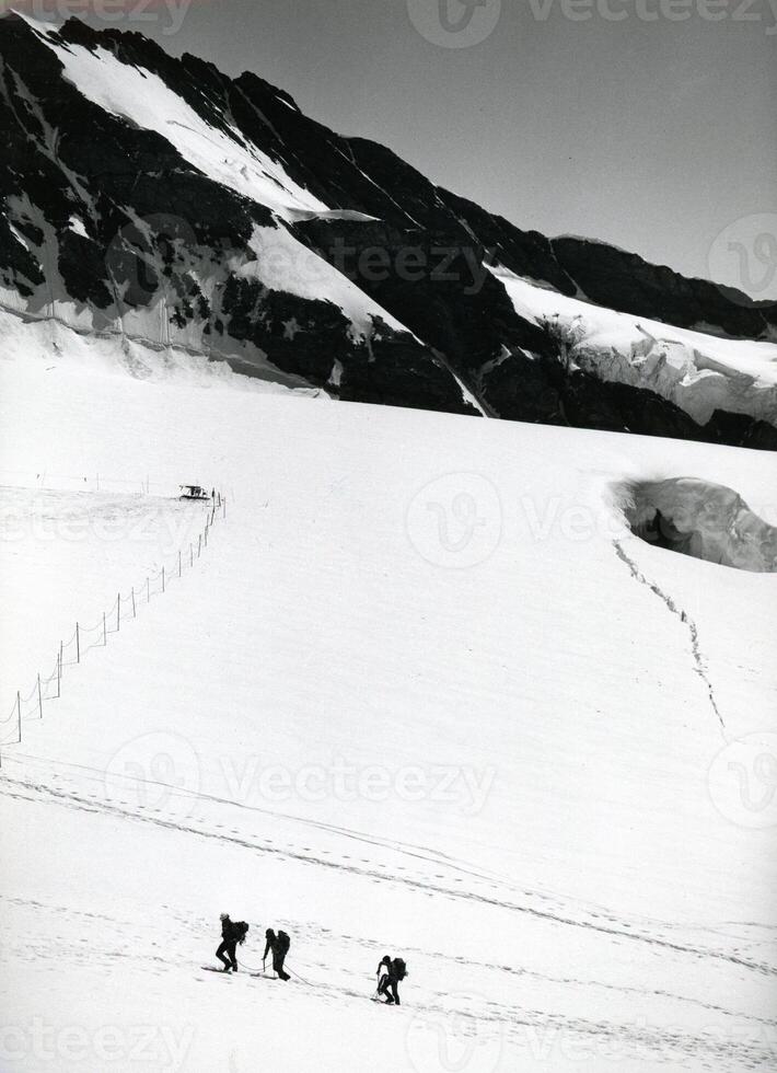 un' gruppo di persone sciare giù un' nevoso pendenza foto