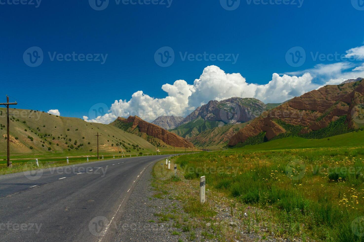 un' sereno paesaggio, con verdeggiante i campi sotto un' blu cielo, affiancato di maestoso montagne e un' serpeggiante strada. foto