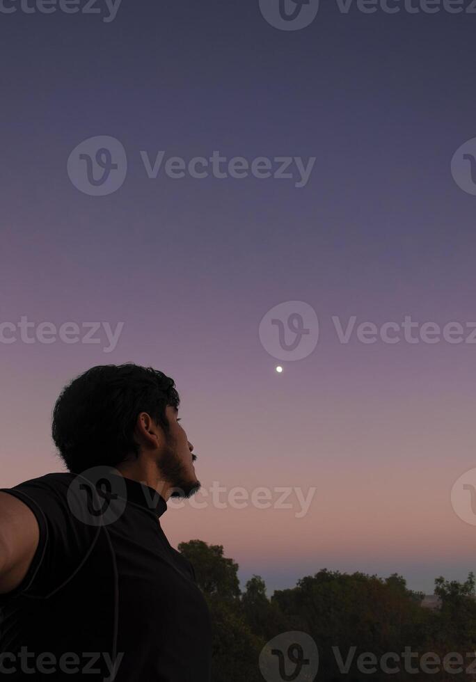 riflessivo uomo guardare a il cielo con bellissimo tramonto nel il sfondo e spazio per testo foto