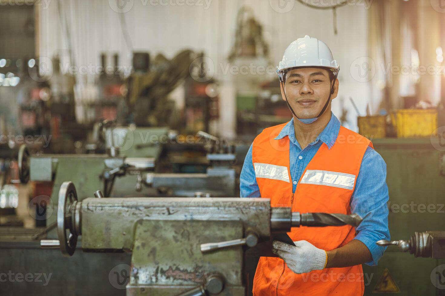 ritratto asiatico ingegnere adulto maschio lavoratore nel macchina negozio con dai un'occhiata elenco contento Sorridi nel sicurezza elmetto protettivo foto