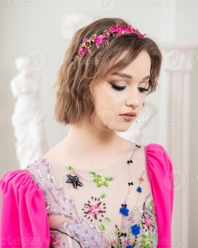 un' ragazza con corto capelli e un' rosa vestito con un' fiore corona su sua testa foto