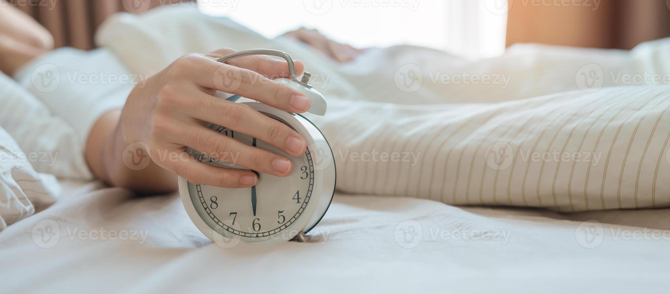 allarme orologio e asiatico donna mano fermare tempo nel letto mentre dormendo, giovane adulto femmina scia su in ritardo nel il presto mattina. rilassante , assonnato, quotidiano routine e avere un' simpatico giorno concetti foto