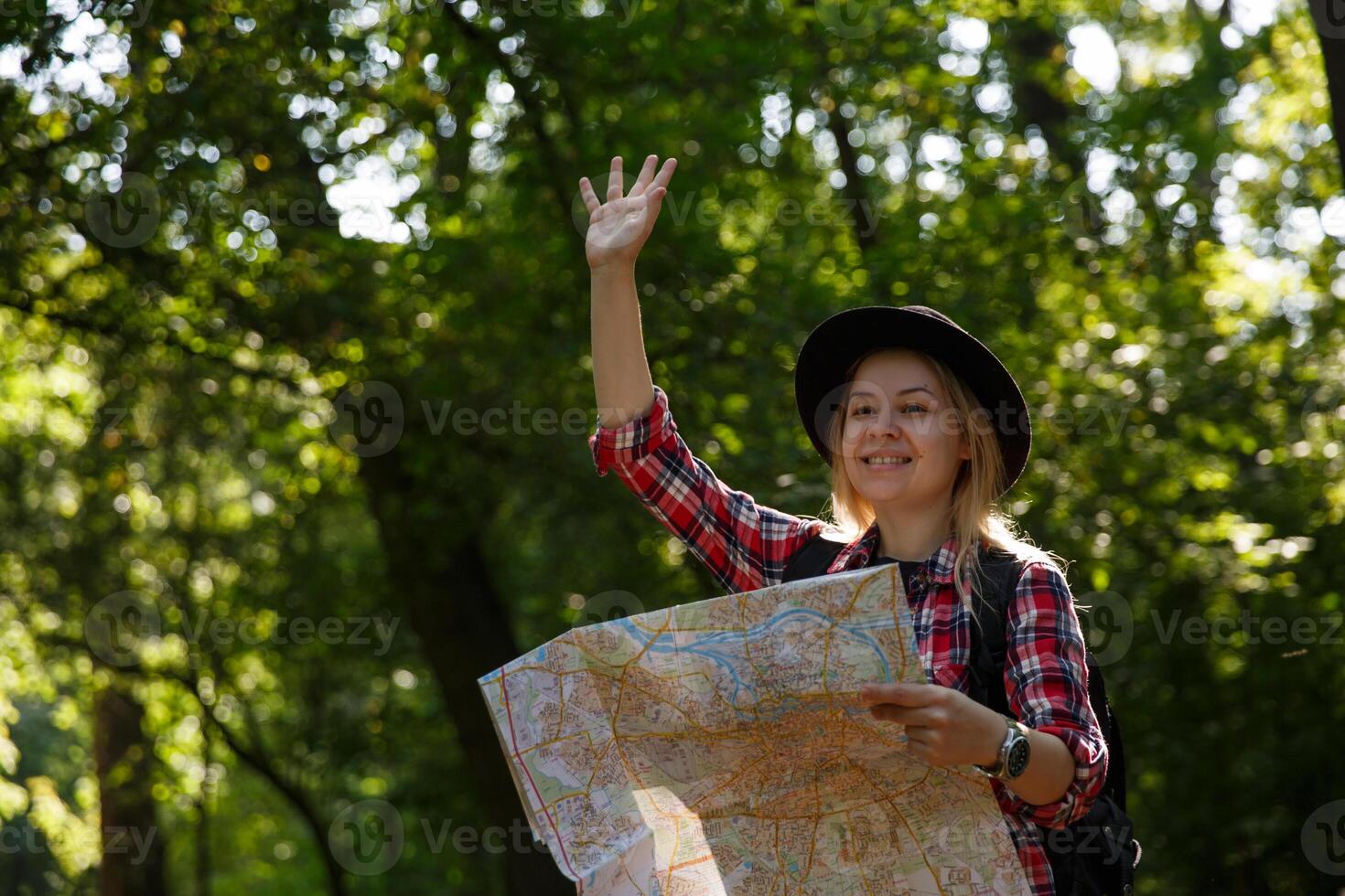 giovane caucasico donna nel un' cappello con un' carta geografica agitando nel saluto. sfocato sfondo, selettivo messa a fuoco. alto qualità foto