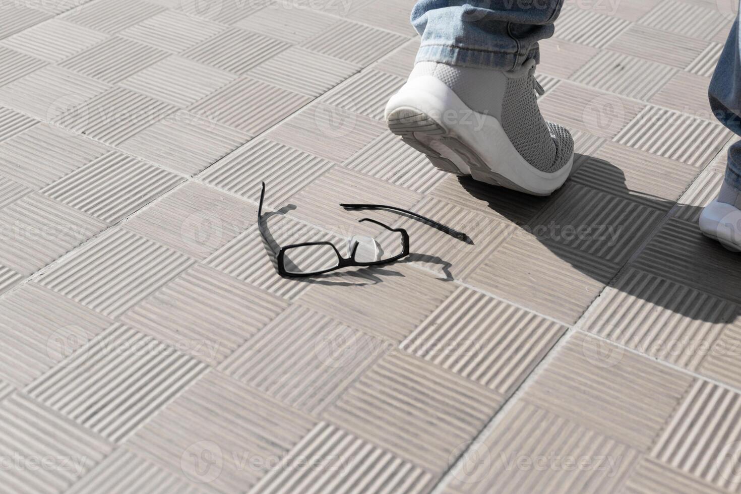 piede nel un' grigio sneaker fatto un passo su il occhiali. rotto bicchiere su strada piastrelle . alto qualità foto