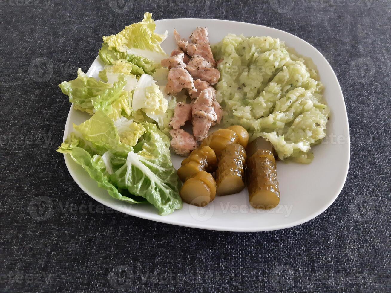 fatti in casa grigliato pollo con zucchine stufato, verde insalata e cetriolo sottaceti servito su un' bianca piatto foto