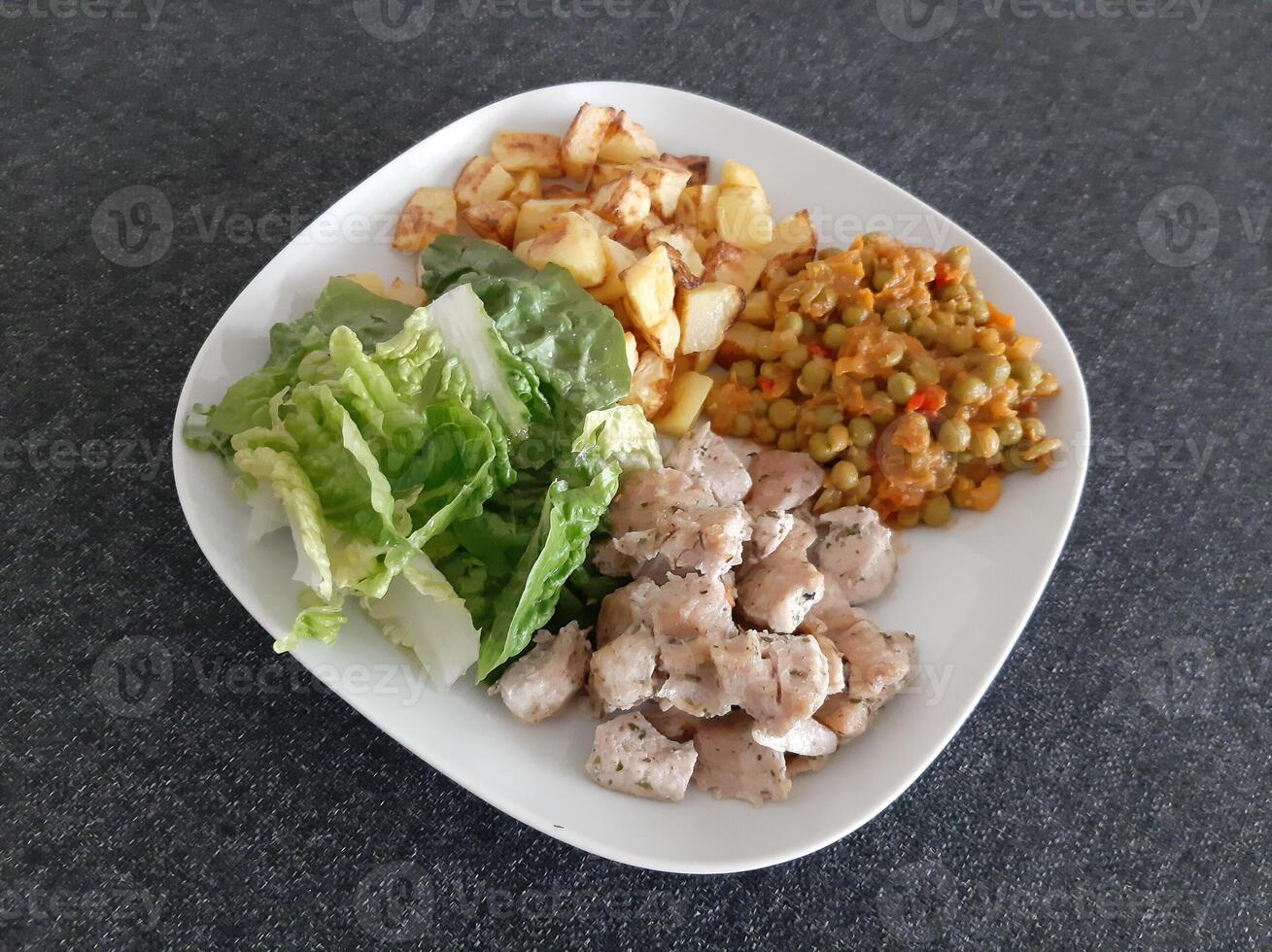 fatti in casa grigliato pollo con francese patatine fritte, verde insalata e pisello stufato servito su un' bianca piatto foto