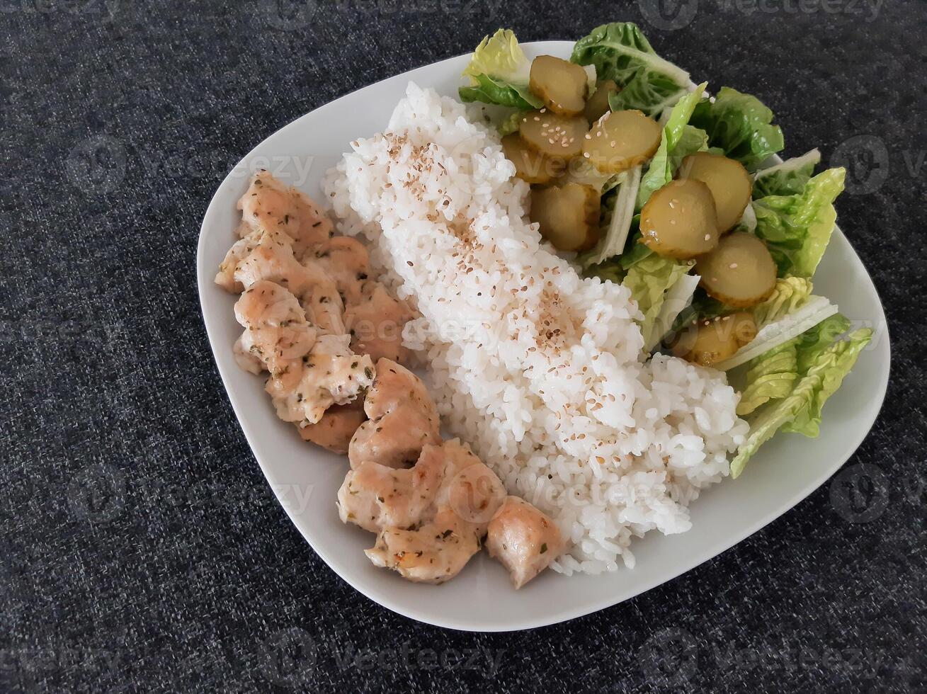 fatti in casa grigliato pollo con verde insalata, riso pilaf e cetriolo sottaceti servito su un' bianca piatto foto