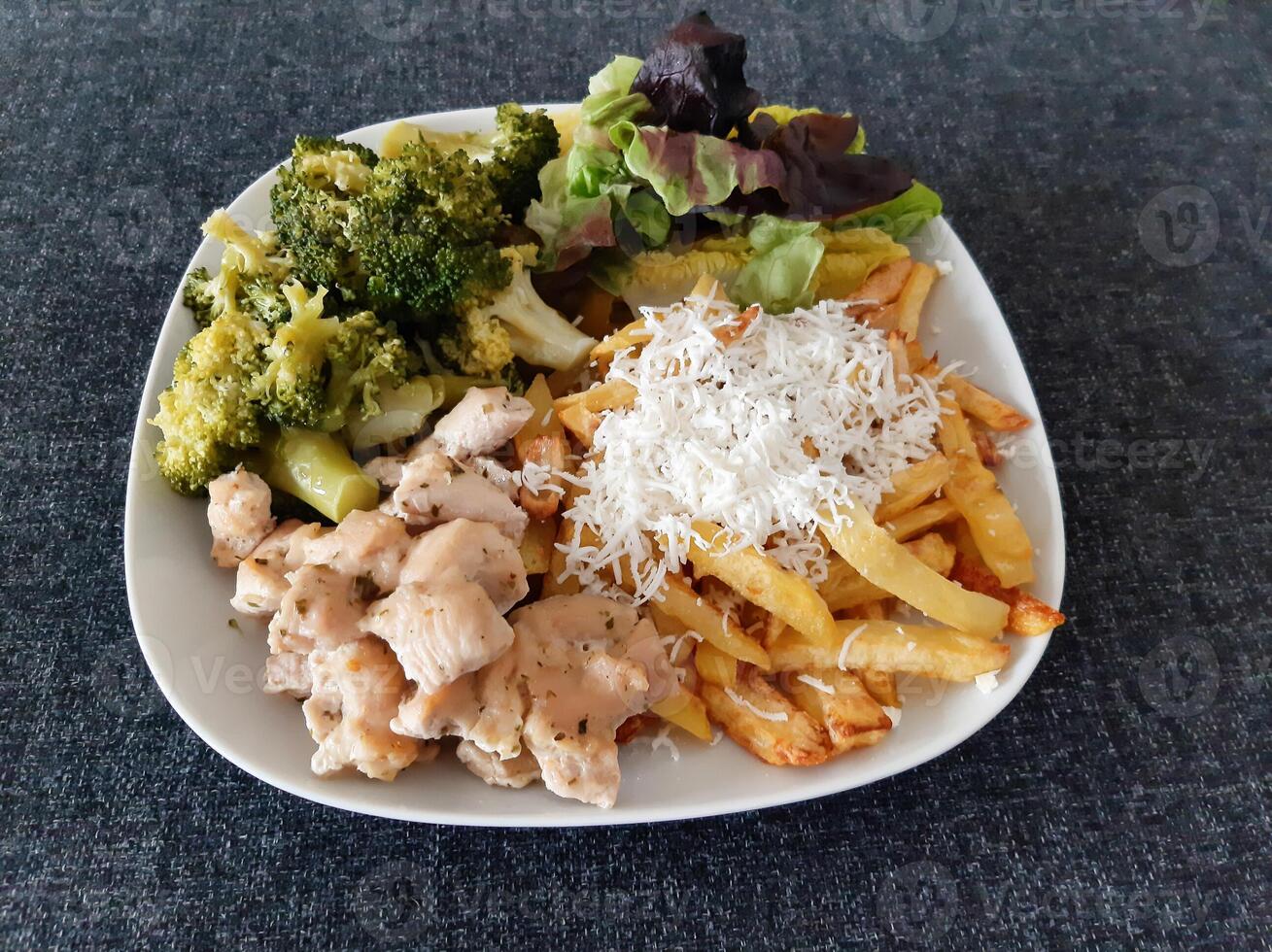 fatti in casa grigliato pollo con francese patatine fritte, broccoli, formaggio e verde insalata, servito su un' bianca piatto foto