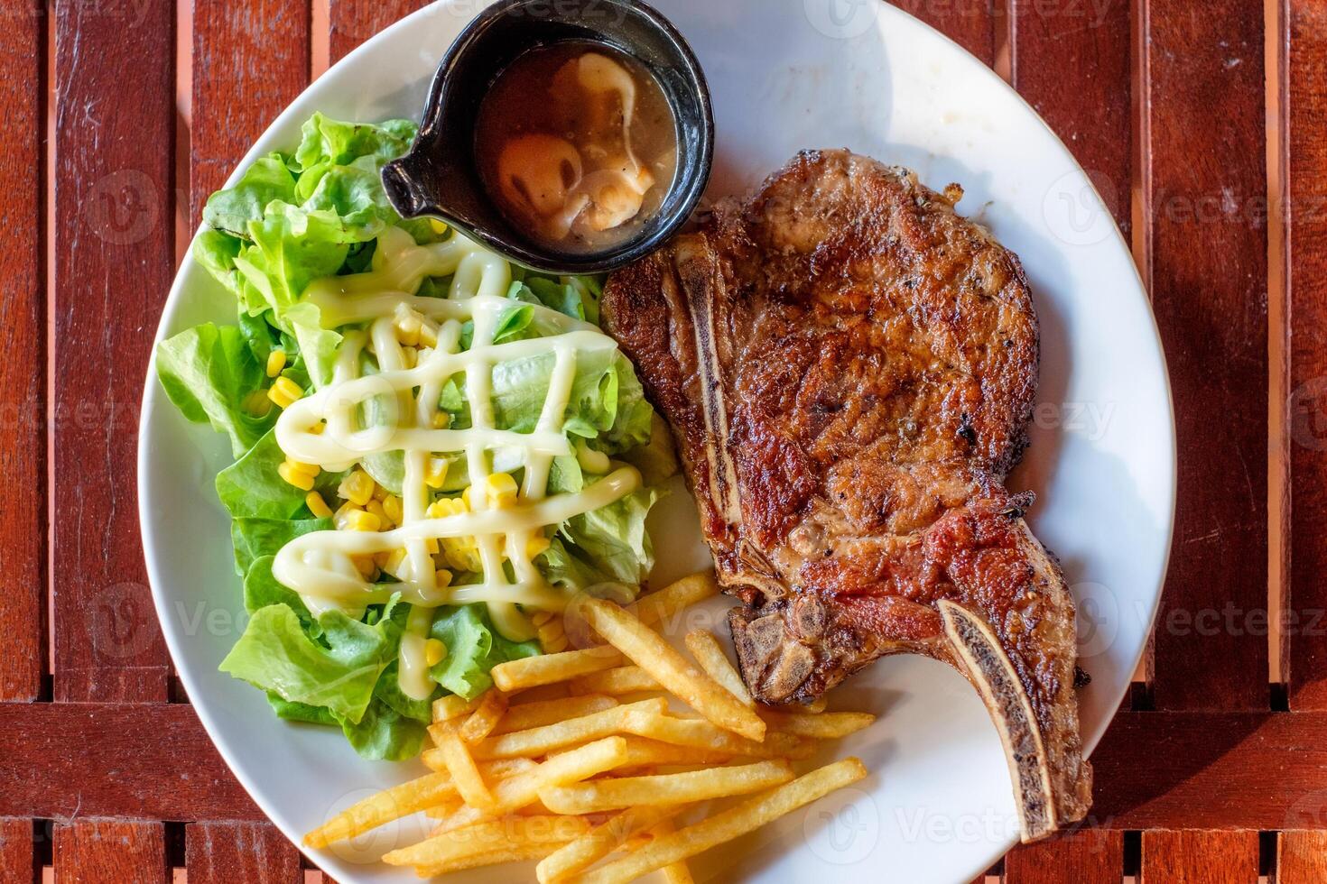 grigliato Maiale costolette bistecca ben fatto con francese patatine fritte e verdura foto