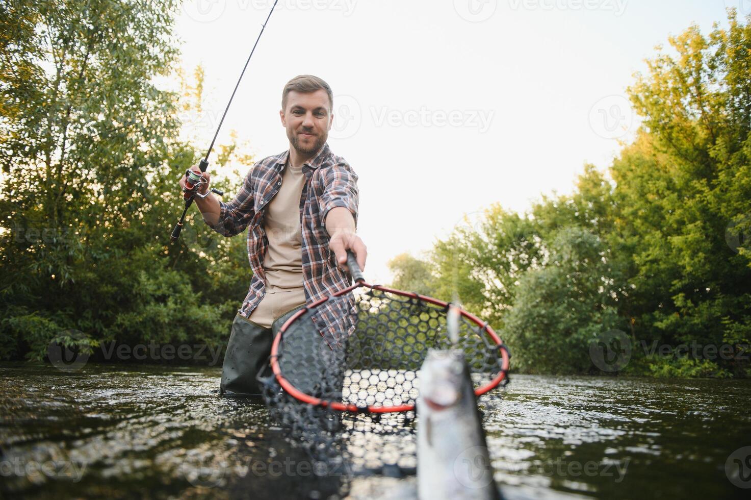 uomo con pesca asta, pescatore uomini nel fiume acqua all'aperto. attraente trota pesce nel rete. estate pesca passatempo foto