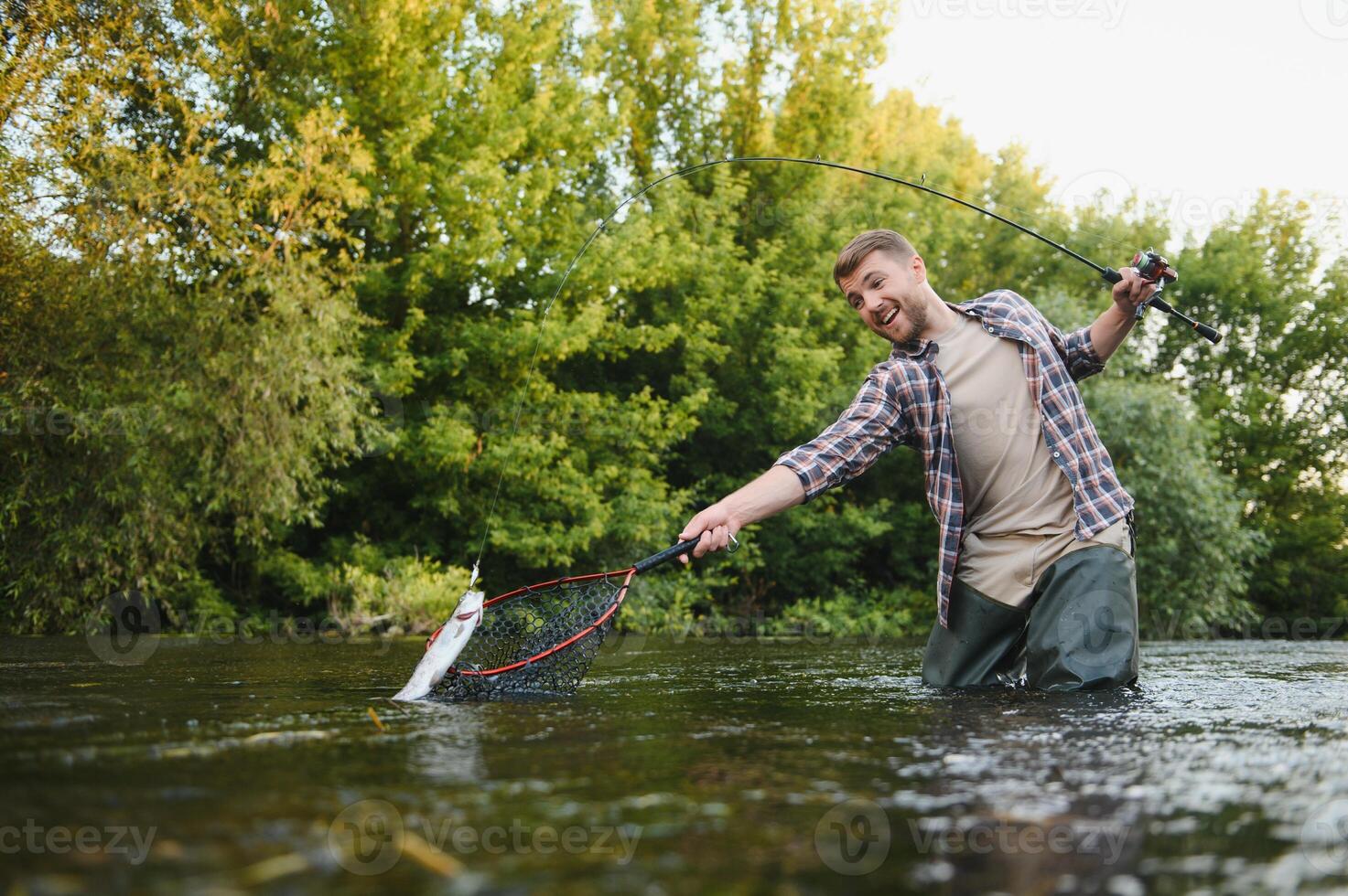 uomo con pesca asta, pescatore uomini nel fiume acqua all'aperto. attraente trota pesce nel rete. estate pesca passatempo foto