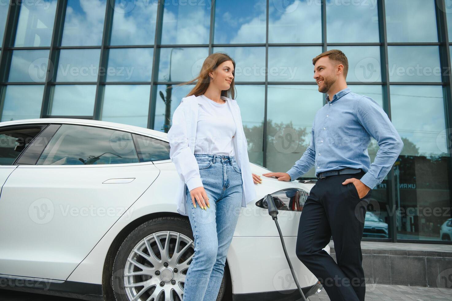 sorridente uomo e donna su il ricarica stazione per elettrico macchine. un' uomo è ricarica un' macchina. foto