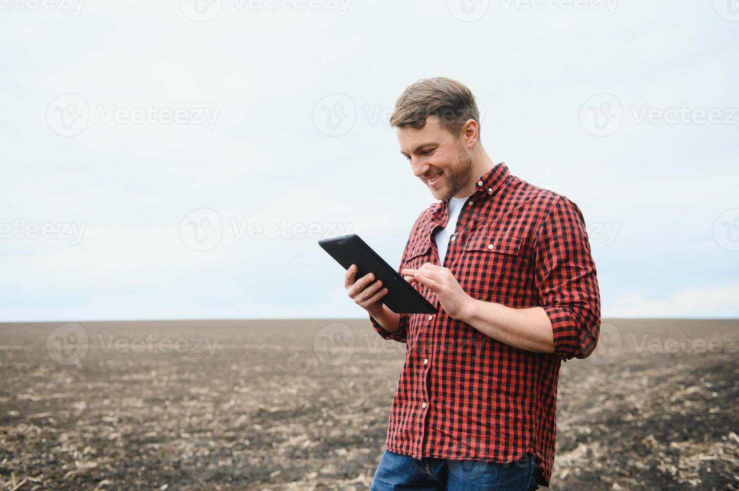 un' contadino nel stivali lavori con il suo tavoletta nel un' campo seminato nel primavera. un agronomo passeggiate il terra, valutare un' arato campo nel autunno. agricoltura. inteligente agricoltura tecnologie foto