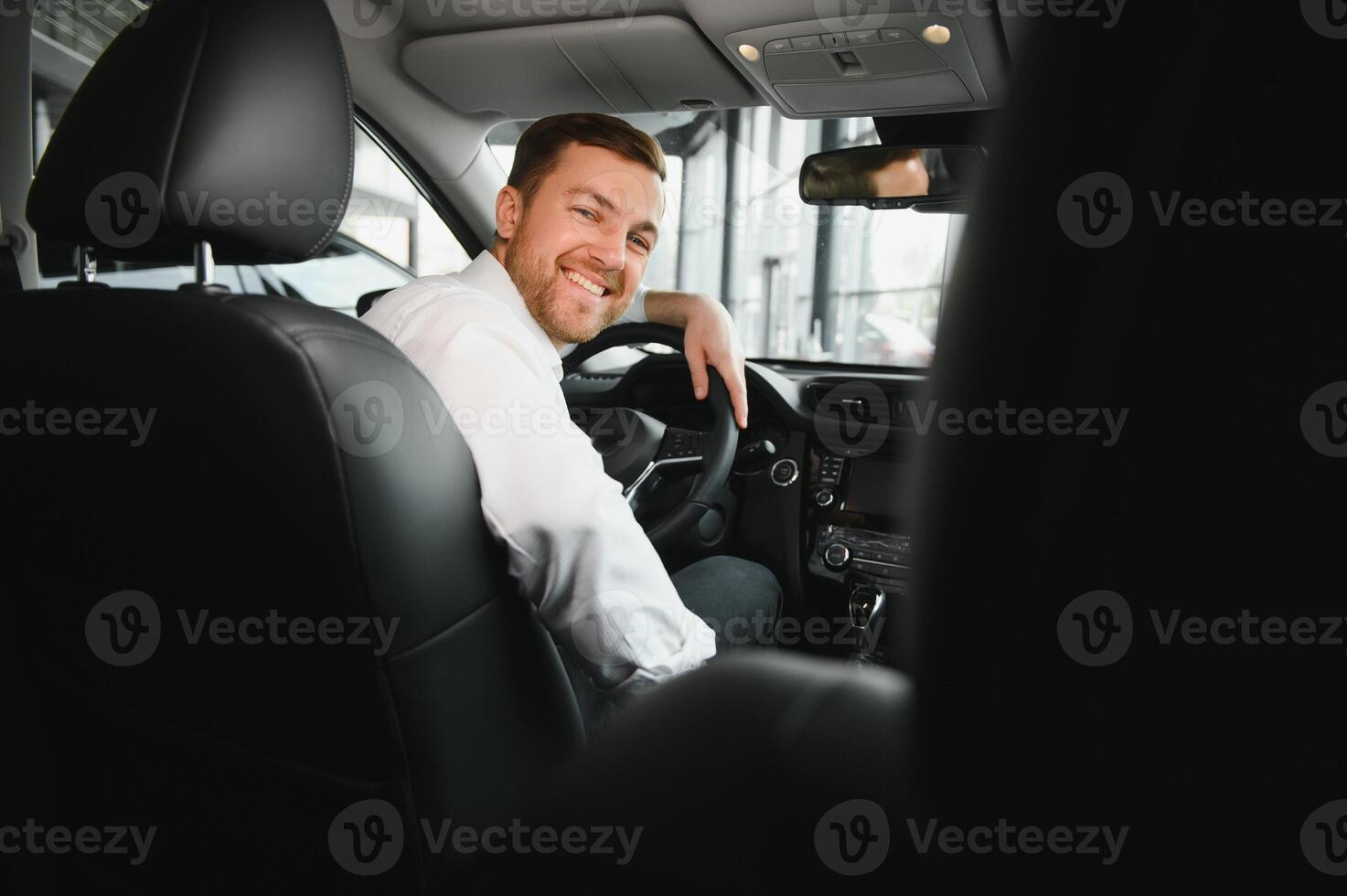 Taxi autista sorridente mentre svolta al di sopra di per il sedile posteriore guardare parlando con clienti. riuscito uomo d'affari marito guardare a il sedile posteriore a commerciante negozio prima acquisto un' auto foto