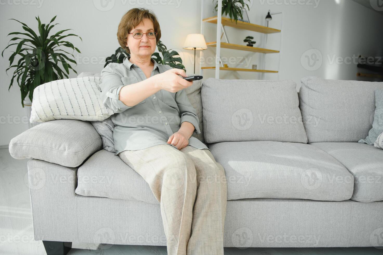 le persone, televisione e divertimento concetto - anziano donna nel occhiali con a distanza controllo Guardando tv a casa foto